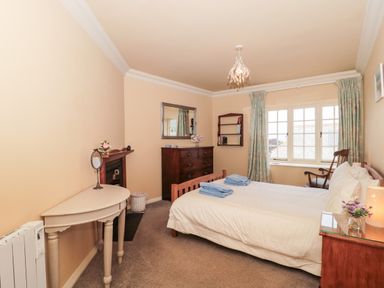A bedroom with a double bed, wooden dresser, corner table, window with curtains, and a rocking chair at The Pound in Porlock