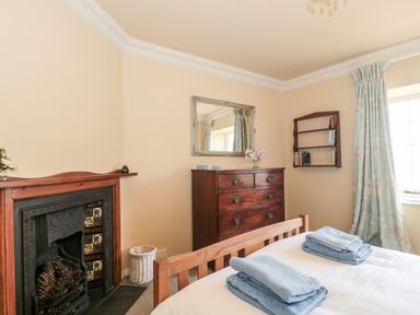 A bedroom with a wooden bed with folded blue towels a wooden chest of drawers a wall mirror a fireplace and a window with blue patterned curtains at The Pound in Porlock