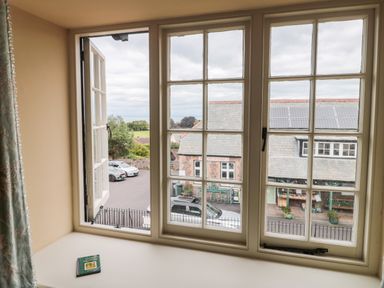 A window with multiple panes looking out onto a street with parked cars and buildings with solar panels on the roofs at The Pound in Porlock