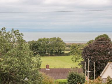 A view of trees fields a roof and the sea in the background at The Pound in Porlock