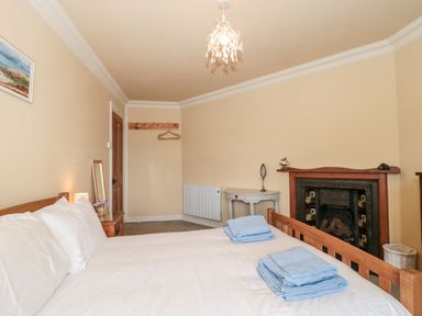 A bedroom with bed linens on a bed a fireplace a small table and a wall-mounted coat rack at The Pound in Porlock