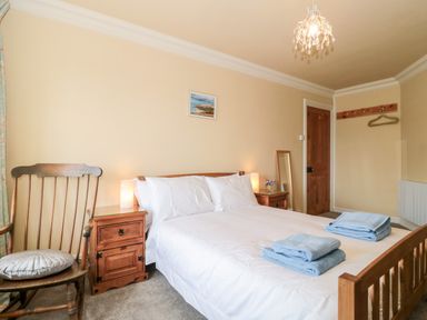 A bedroom with a wooden bed with white bedding and blue towels on it a wooden rocking chair beside a wooden nightstand with a lamp and a picture on the wall at The Pound in Porlock