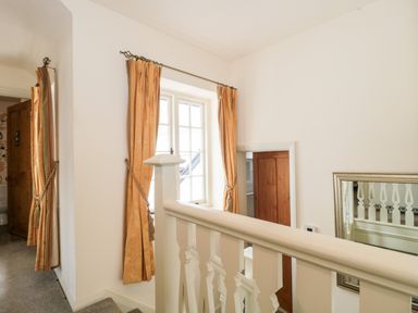 A hallway with stairs a window with curtains a mirror and wooden doors at The Pound in Porlock