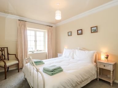 A bedroom with a white bed and folded towels on it next to a window with curtains and a wooden chair at The Pound in Porlock
