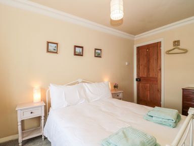 A bedroom with a white bed, bedside tables with lamps, three small framed pictures on the wall, a wooden door, and folded towels on the bed at The Pound in Porlock