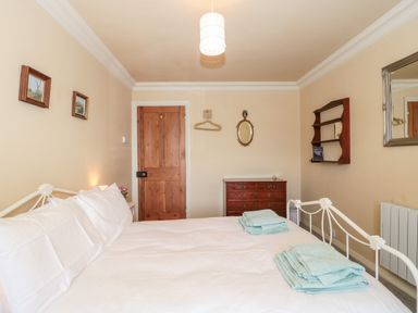 A bedroom with a neatly made bed with folded towels on it a wooden door a wooden chest of drawers and wall shelves at The Pound in Porlock