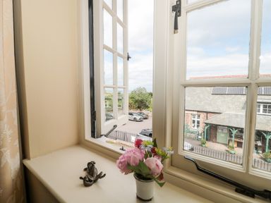 An open window with a small flower pot and a frog ornament on the windowsill overlooking a parking area and building with solar panels at The Pound in Porlock