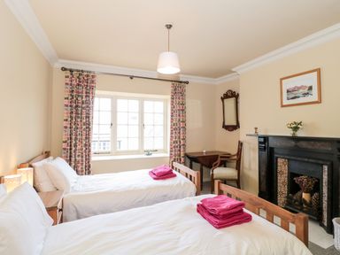 A bedroom with two single beds with folded pink towels on top a window with patterned curtains a black fireplace a wooden chair wooden table and a wall mirror at The Pound in Porlock