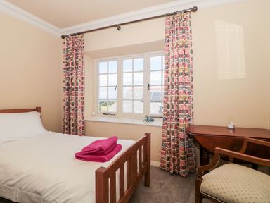 A bedroom with a wooden bed with white bedding and pink towels by a window with patterned curtains and a wooden desk with a chair at The Pound in Porlock