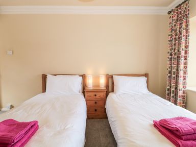 A bedroom with two single beds white bedding pink towels bedside table with lamps and patterned curtains at The Pound in Porlock