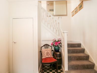 A staircase with carpeted steps a wooden chair with cushion and a vase with flowers on a barrel at The Pound in Porlock