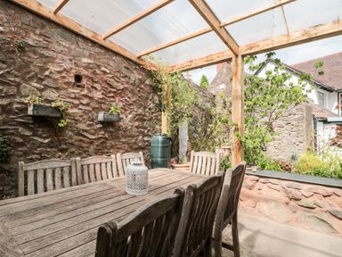 An outdoor dining area with a wooden table and chairs under a transparent roof at The Pound in Porlock