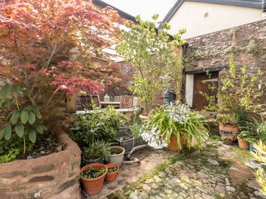 An outdoor patio with various plants in pots and planters surrounded by stone walls and a wooden dining table with chairs at The Pound Porlock