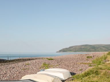A pebble beach with overturned boats and hills in the distance at The Pound in Porlock
