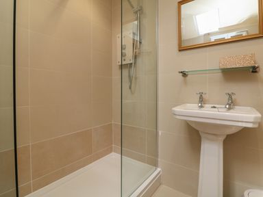 A bathroom with a glass shower enclosure and a pedestal sink with taps and a mirror above at The Pound in Porlock