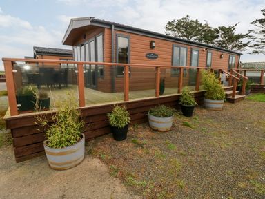 A wooden cabin with glass railing and potted plants outside at Reef Retreat Broad Haven