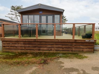 A wooden lodge with glass doors and windows and a glass-paneled deck at Reef Retreat in Broad Haven