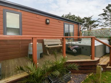 An outdoor wooden deck with glass railing a bench a barrel a hot tub and plants at Reef Retreat Broad Haven