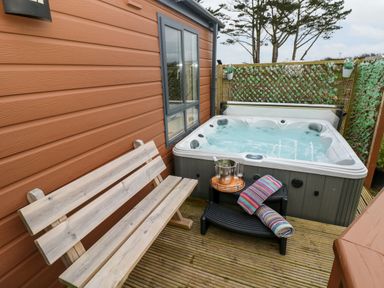 An outdoor area with a wooden bench a hot tub a small table with a bucket and glasses and a rolled towel on a chair at Reef Retreat in Broad Haven