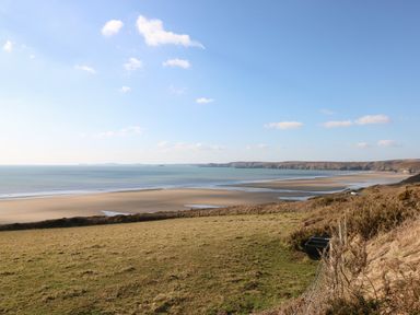 A coastal landscape with grassy land overlooking a wide sandy beach and ocean at Reef Retreat in Broad Haven