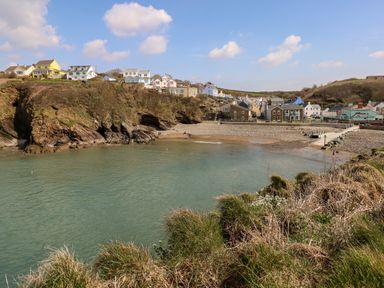 A coastal village with houses on cliffs and a small beach at Reef Retreat in Broad Haven