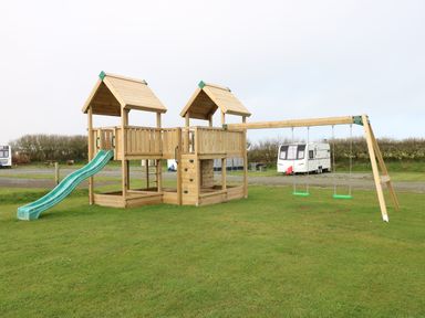 A wooden playground structure with two slides and two swings on a grassy field at Reef Retreat in Broad Haven