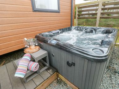An outdoor hot tub with bubbling water next to a wooden wall with a small wooden step holding a tray with a bottle on ice and four glasses and two rolled towels at Seahorse Retreat in Little Haven near Broad Haven