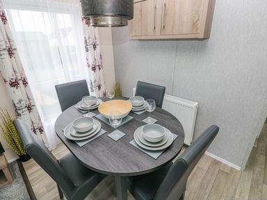 A dining area with a round table set with plates bowls and glasses four chairs and a window with patterned curtains at Seahorse Retreat in Little Haven near Broad Haven