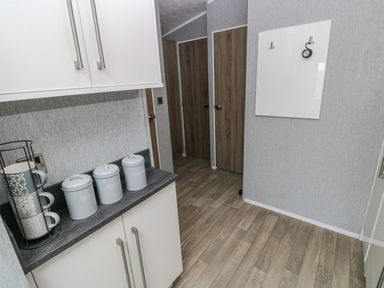 A kitchen corner with white cabinets three labeled canisters and three hanging mugs at Seahorse Retreat in Little Haven near Broad Haven