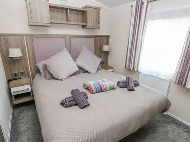 A bedroom with a double bed two pillows rolled towels bedside tables and a window with curtains at Seahorse Retreat in Little Haven near Broad Haven