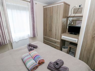 A bedroom with a bed and rolled towels a wooden wardrobe and a desk with a TV at Seahorse Retreat in Little Haven near Broad Haven