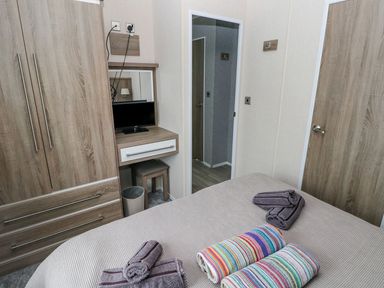 A bedroom with a bed covered in towels a wooden wardrobe a small desk with a mirror and a TV at Seahorse Retreat in Little Haven near Broad Haven