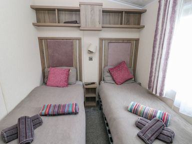 A bedroom with two single beds each with a pink pillow folded towels bedside table and wall shelves at Seahorse Retreat in Little Haven near Broad Haven