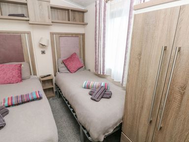A bedroom with two single beds with pink cushions and folded towels near a wooden wardrobe at Seahorse Retreat in Little Haven near Broad Haven