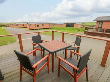 A wooden deck with a square table and four wicker chairs overlooking mobile homes and grassy fields at Seahorse Retreat in Little Haven near Broad Haven