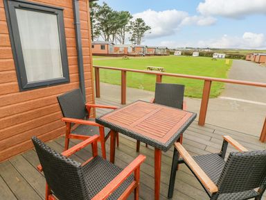 A wooden deck with table and four chairs outside wooden lodges at Seahorse Retreat in Little Haven near Broad Haven