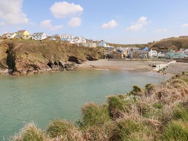 A coastal village with houses on a hill overlooking a small sandy beach and calm sea at Seahorse Retreat in Little Haven near Broad Haven