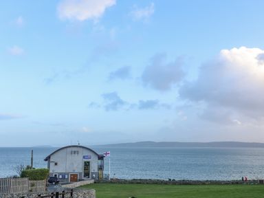 A lifeboat station building by the sea with a flagpole and a grassy area at Haulfryn in Moelfre