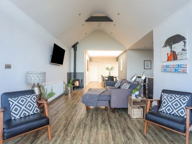 A living room with chairs pillows a sofa a TV and a dining table at Haulfryn in Moelfre