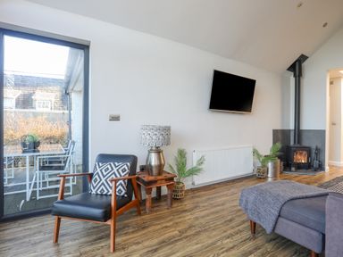 A living room with a black armchair wooden side table lamp wall mounted tv wood stove and glass door to patio at Haulfryn in Moelfre