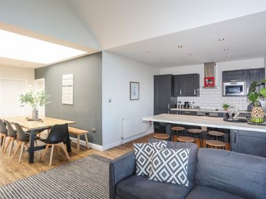 An open plan kitchen and dining area with a wooden dining table and chairs and a kitchen island with stools at Haulfryn in Moelfre