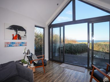 A living room with large glass sliding doors and black chairs overlooking a sea view at Haulfryn in Moelfre