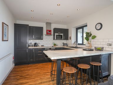 A kitchen with dark cabinets wooden stools and a marble countertop at Haulfryn in Moelfre