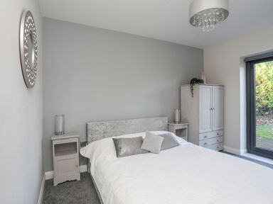 A bedroom with a bed with white bedding gray pillows two nightstands with lamps a wardrobe and a large window at Haulfryn in Moelfre