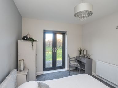 A bedroom with a gray desk and chair near glass doors opening to a garden at Haulfryn in Moelfre