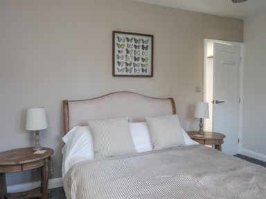 A bedroom with a bed two bedside tables with lamps and butterfly wall art at Haulfryn in Moelfre