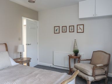 A bedroom with a bed table lamp armchair and framed pictures on the wall at Haulfryn in Moelfre