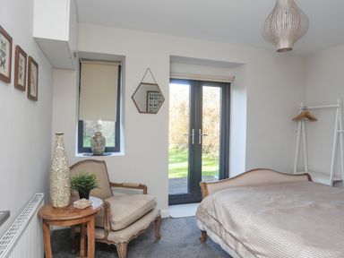 A bedroom with a bed armchair side table and double doors leading outside at Haulfryn in Moelfre