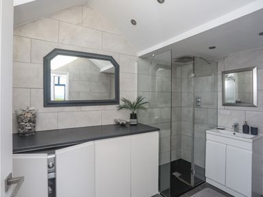 A bathroom with a glass shower enclosure a sink cabinet and a large mirror at Haulfryn in Moelfre