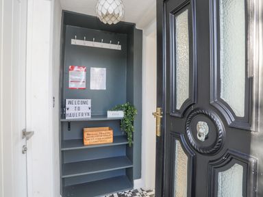 A small entryway with shelves a welcome sign and a black front door at Haulfryn in Moelfre